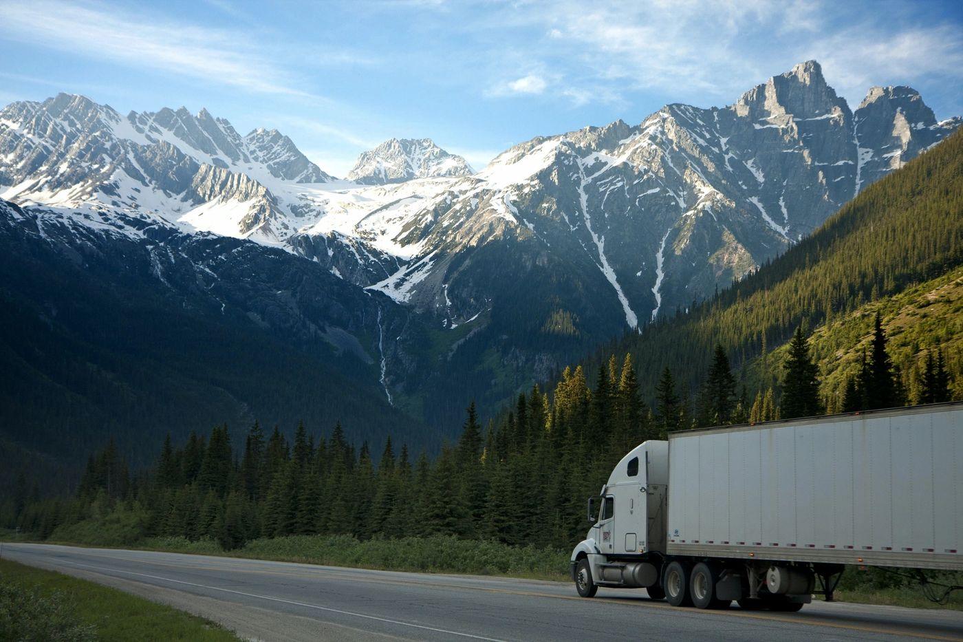 A semi truck on a highway through snow-capped mountains